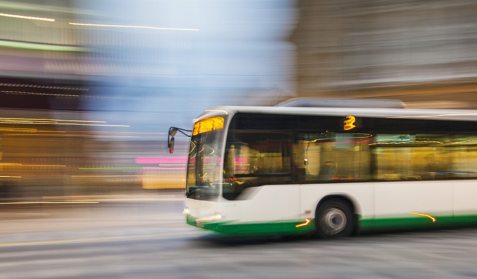 Motion-blurred city transit bus driving past illuminated storefronts
